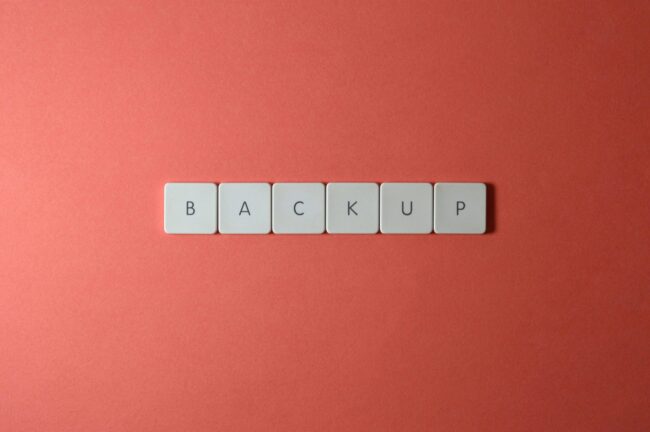 Free Close-up of keyboard keys spelling 'BACKUP' placed on a coral-colored surface. Stock Photo