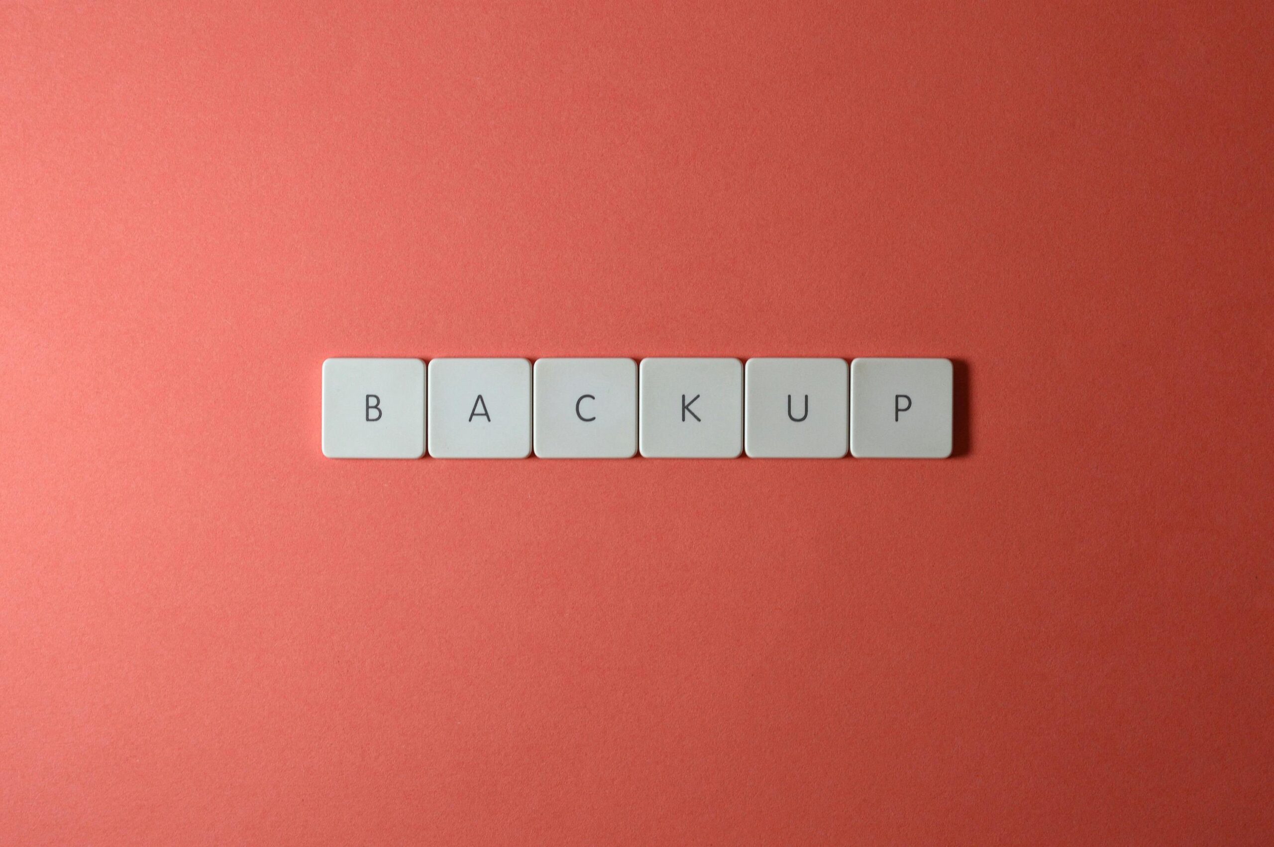 Simple-Backup-and-Recovery-Plans-Every-Small-Business-Needs-scaled.jpg - Technovation Free Close-up of keyboard keys spelling 'BACKUP' placed on a coral-colored surface. Stock Photo