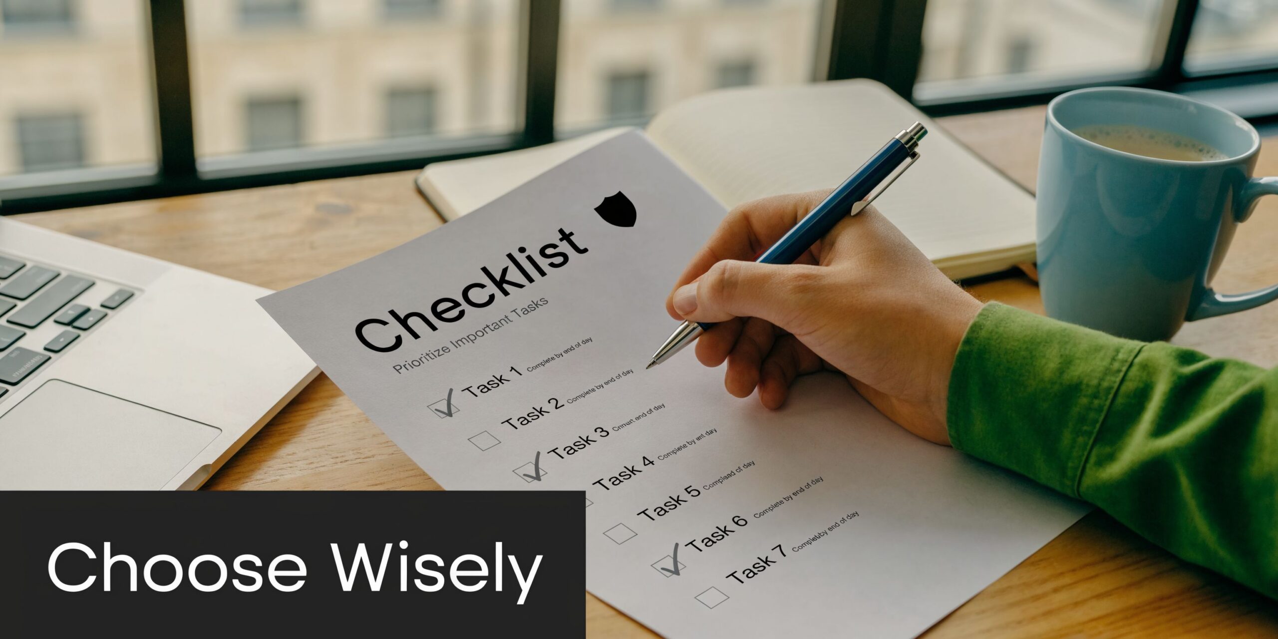 A person hand checking items off a professional cybersecurity checklist on a wooden desk with a laptop.