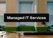 Banner reads 'Managed IT Services' over a modern office desk with a keyboard, stethoscope, and laptop in the background.