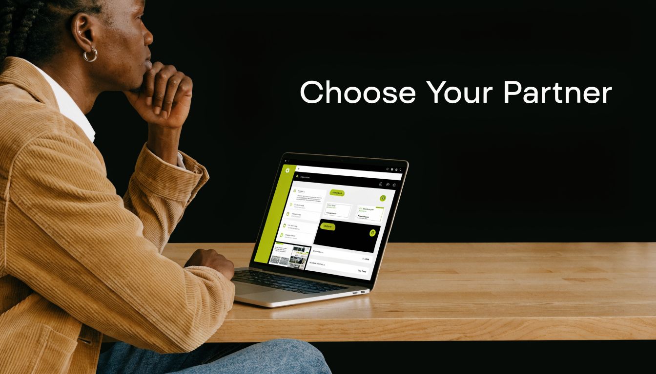 A person sitting at a wooden desk, looking thoughtfully at a laptop screen displaying software interface options.