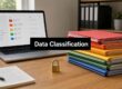 Desk setup illustrating data classification: laptop with a file browser, a padlock, and a rainbow stack of colored folders labeled Data Classification.
