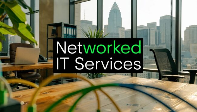 networked-it-services-office-workspace Office with a laptop on a wooden desk and a bold black sign that reads 'Networked IT Services' against a city skyline window backdrop