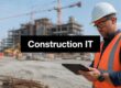 Construction worker in a high-visibility vest and white hard hat inspecting a tablet at a construction site, with a building under construction in the background.