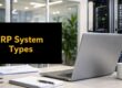 Office desk scene with a silver laptop, notebook, and mug; a black monitor or screen reads 'ERP System Types' in yellow.