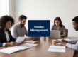 Team of four in a meeting around a conference table discussing documents with a 'Vendor Management' sign in the center. (Informative)
