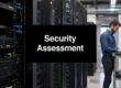 Server racks in a data center with a large sign reading 'Security Assessment' and a technician using a laptop at a mobile workstation nearby