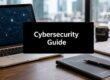 Laptop on a wooden desk with a black sign reading 'Cybersecurity Guide' in front of a security-themed screen and office items nearby.