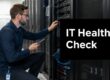 IT professional checks server equipment in a data center, holding a tablet and inspecting rack-mounted hardware under a bold 'IT Health Check' overlay.