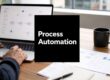 Person typing on a laptop at a desk with a black card reading 'Process Automation' in the foreground.